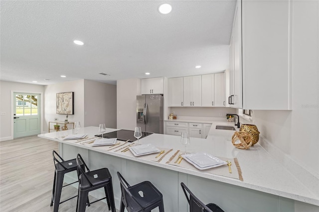 kitchen featuring a peninsula, a breakfast bar, stainless steel refrigerator with ice dispenser, and white cabinets