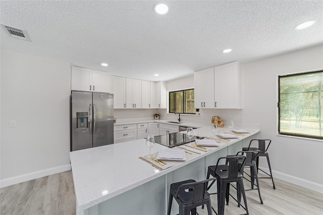 kitchen featuring a breakfast bar area, white cabinets, a sink, stainless steel fridge, and a peninsula