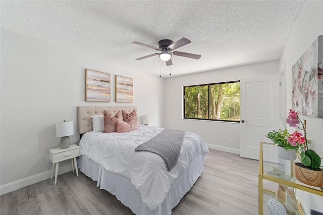 bedroom with light wood-style floors, a ceiling fan, baseboards, and a textured ceiling