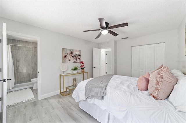 bedroom featuring visible vents, ensuite bath, light wood-style flooring, a textured ceiling, and a closet