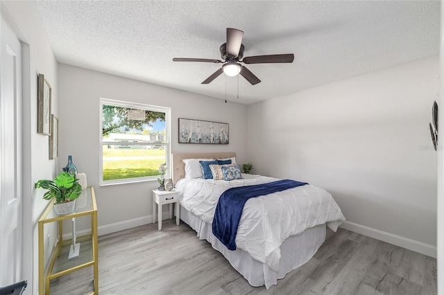 bedroom with light wood-style floors, baseboards, and a textured ceiling