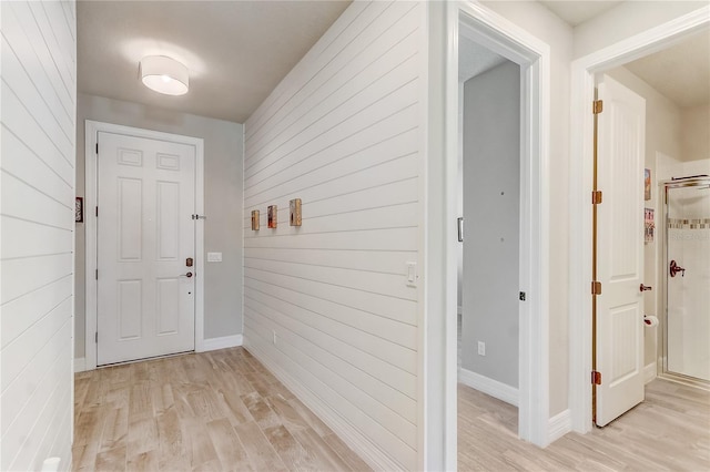 hallway featuring light wood-type flooring and wooden walls