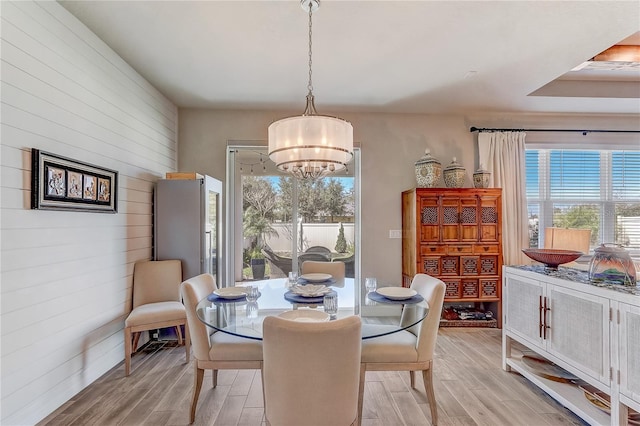 dining area featuring wood walls, light wood-style flooring, and a notable chandelier