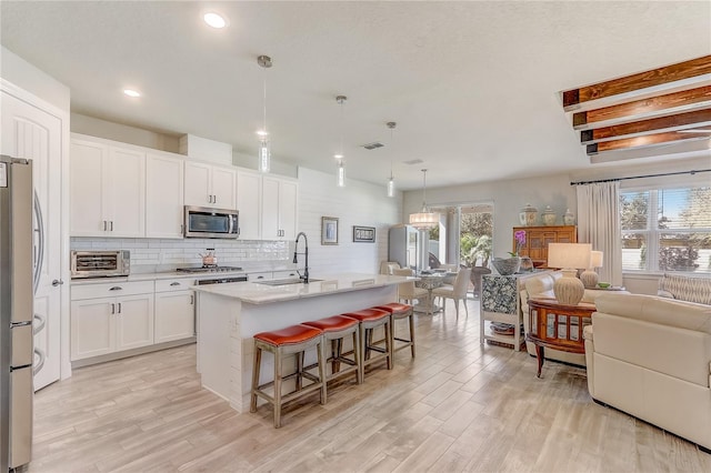 kitchen featuring a center island with sink, white cabinets, appliances with stainless steel finishes, hanging light fixtures, and a sink