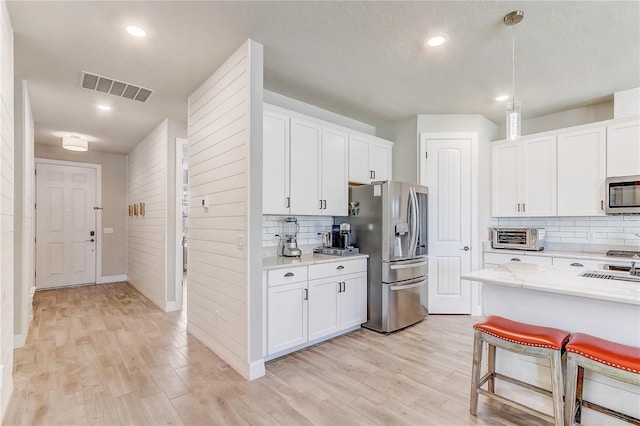 kitchen with hanging light fixtures, appliances with stainless steel finishes, visible vents, and white cabinets