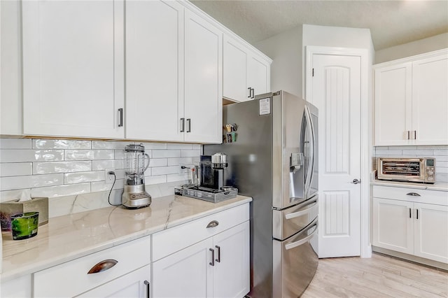 kitchen featuring backsplash, white cabinetry, stainless steel refrigerator with ice dispenser, and light stone countertops