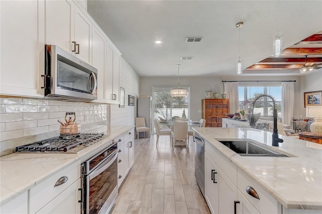 kitchen featuring stainless steel appliances, a sink, white cabinets, decorative backsplash, and decorative light fixtures