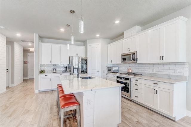 kitchen with appliances with stainless steel finishes, a kitchen island with sink, and white cabinets