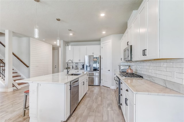 kitchen with stainless steel appliances, white cabinetry, a sink, and an island with sink