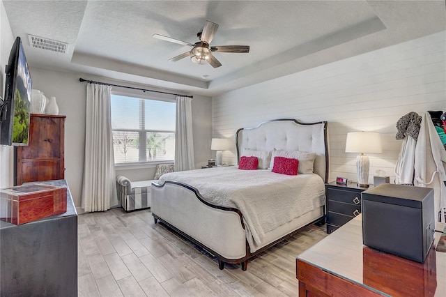 bedroom with a tray ceiling, visible vents, a textured ceiling, and wood finished floors