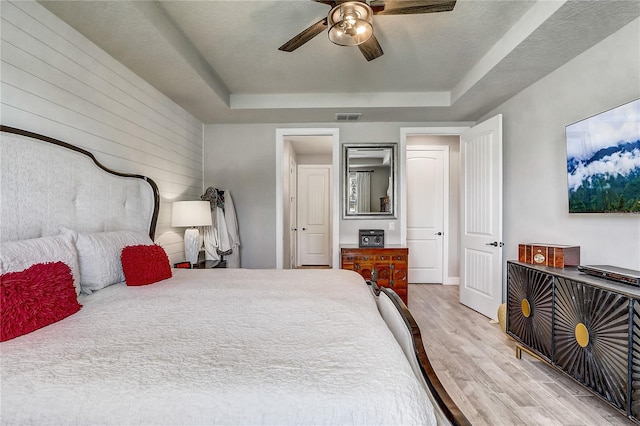 bedroom featuring light wood finished floors, visible vents, a raised ceiling, and a ceiling fan