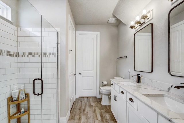 full bathroom with a stall shower, a sink, toilet, and wood finished floors