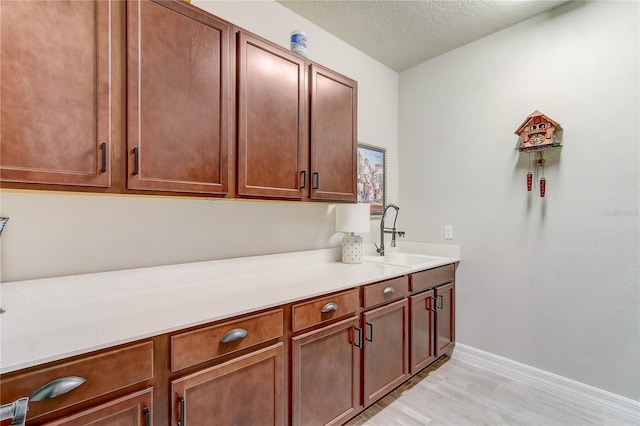 laundry area with light wood-style flooring, a textured ceiling, baseboards, and a sink