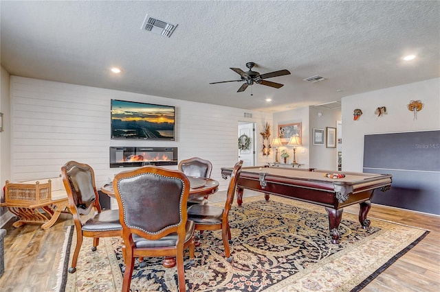 recreation room featuring a textured ceiling, a ceiling fan, visible vents, and light wood-style floors