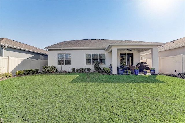 rear view of property featuring a fenced backyard, a lawn, a ceiling fan, and stucco siding