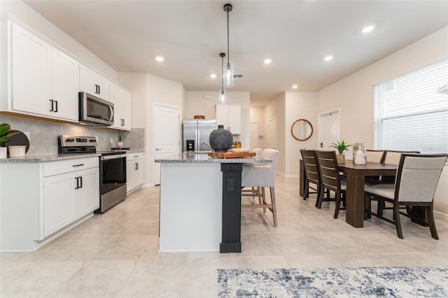 kitchen featuring tasteful backsplash, appliances with stainless steel finishes, white cabinets, an island with sink, and a kitchen bar