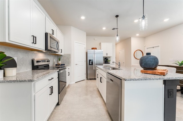 kitchen with decorative backsplash, appliances with stainless steel finishes, white cabinets, a sink, and an island with sink