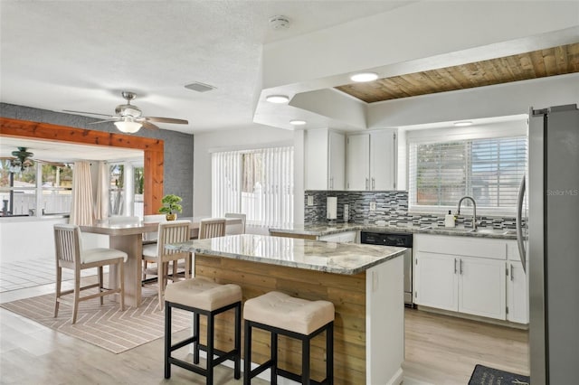 kitchen featuring light stone counters, backsplash, appliances with stainless steel finishes, white cabinetry, and a sink