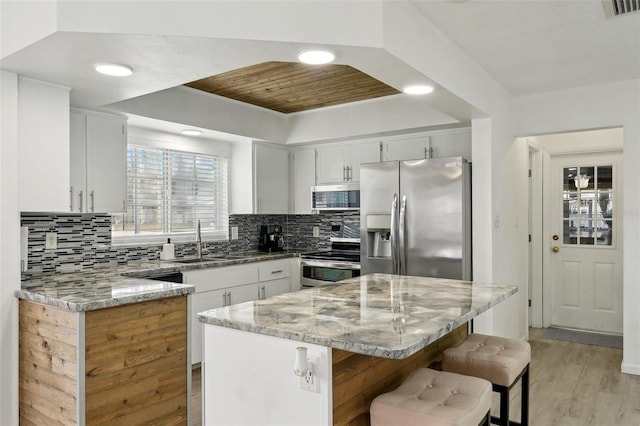 kitchen featuring white cabinets, light stone counters, a center island, stainless steel appliances, and a sink