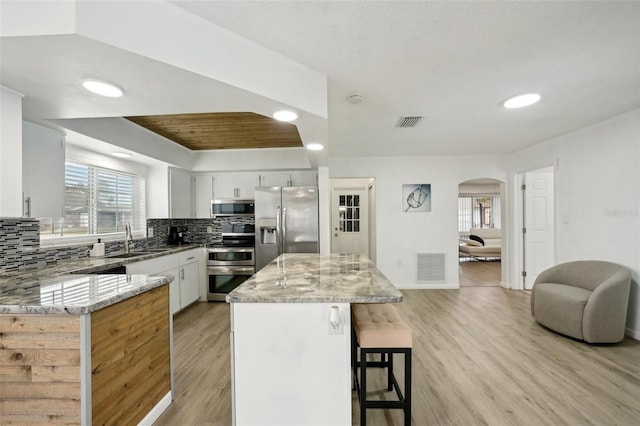 kitchen with light stone counters, stainless steel appliances, visible vents, white cabinetry, and a kitchen island