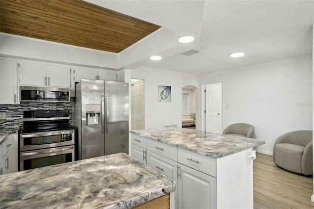 kitchen with a center island, visible vents, decorative backsplash, appliances with stainless steel finishes, and light stone countertops