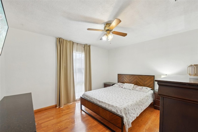 bedroom featuring a textured ceiling, light wood-type flooring, a ceiling fan, and baseboards