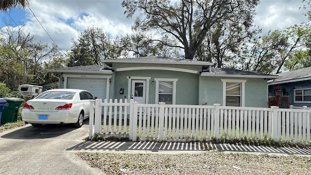 view of front facade featuring driveway, a fenced front yard, an attached garage, and stucco siding