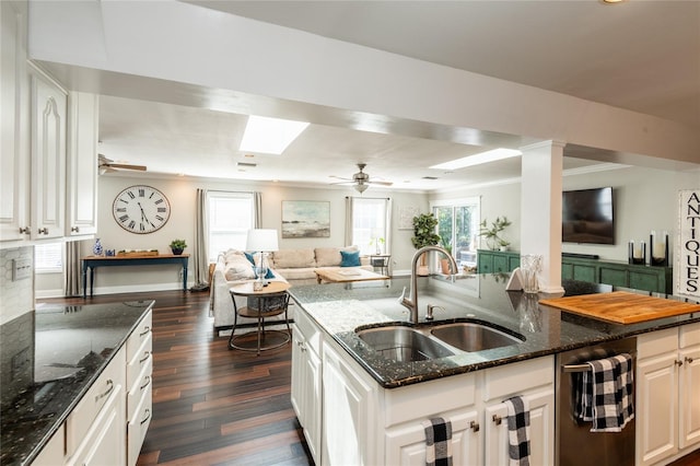 kitchen featuring open floor plan, white cabinets, a sink, a healthy amount of sunlight, and dark stone counters