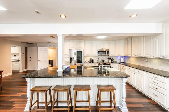 kitchen with white cabinets, a kitchen island with sink, stainless steel appliances, and dark stone countertops