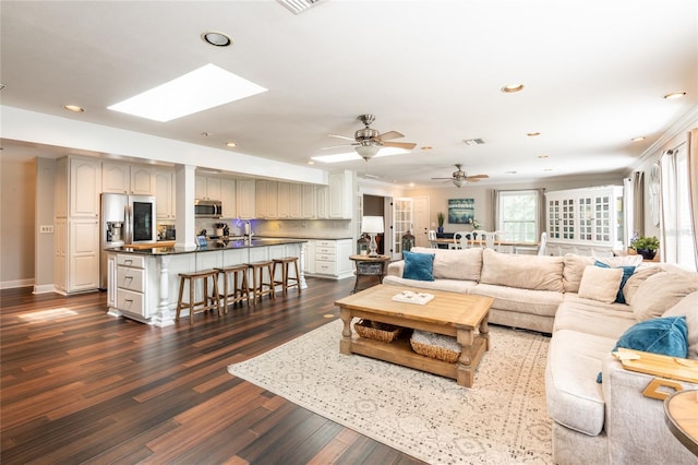 living room featuring a skylight, baseboards, visible vents, dark wood-style flooring, and recessed lighting