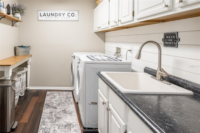 washroom featuring cabinet space, baseboards, dark wood-style flooring, washing machine and clothes dryer, and a sink