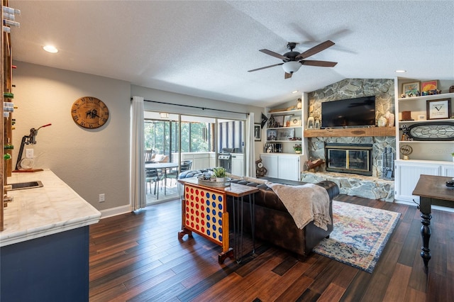 living room featuring dark wood finished floors, lofted ceiling, ceiling fan, a stone fireplace, and a textured ceiling