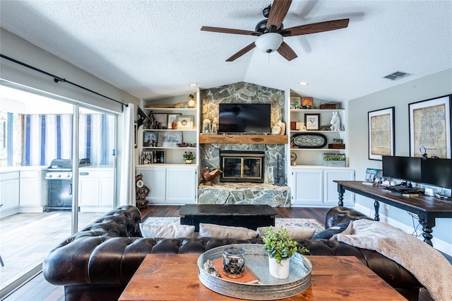 living area featuring a fireplace, visible vents, light wood-style floors, vaulted ceiling, and a textured ceiling