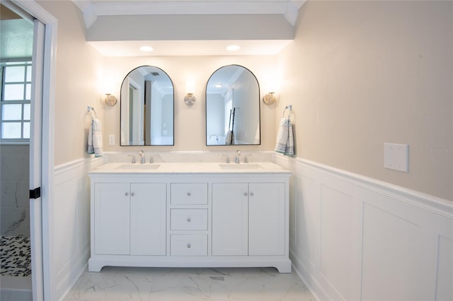 bathroom featuring marble finish floor, a wainscoted wall, a sink, and double vanity