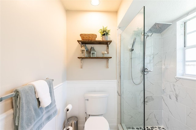 full bathroom with a wainscoted wall, a marble finish shower, toilet, and a decorative wall