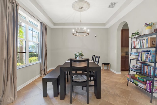 dining space featuring baseboards, visible vents, arched walkways, a tray ceiling, and a notable chandelier