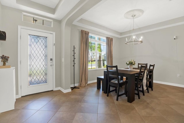 tiled dining space featuring baseboards, a raised ceiling, and a chandelier