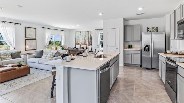 kitchen featuring a center island with sink, stainless steel appliances, sink, gray cabinets, and light tile patterned floors