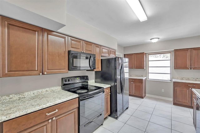 kitchen with light tile patterned floors, light stone countertops, and black appliances