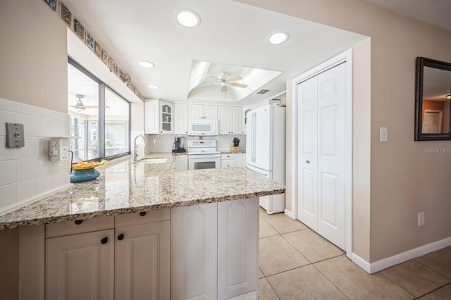 kitchen with white appliances, glass insert cabinets, a peninsula, light stone countertops, and white cabinetry