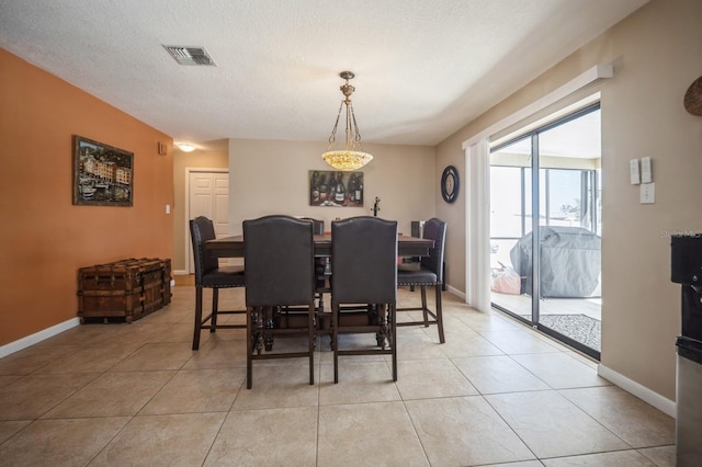 dining space with a textured ceiling, light tile patterned floors, visible vents, and baseboards