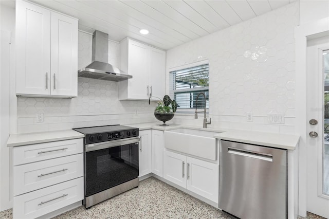 kitchen with stainless steel appliances, a sink, white cabinetry, light countertops, and wall chimney exhaust hood