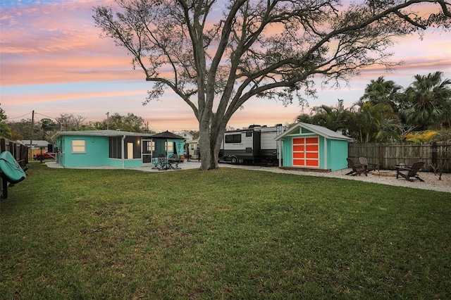 yard at dusk with a patio area, fence, a storage unit, and an outdoor structure