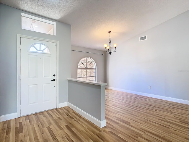 entrance foyer with light wood-type flooring, a textured ceiling, and a notable chandelier