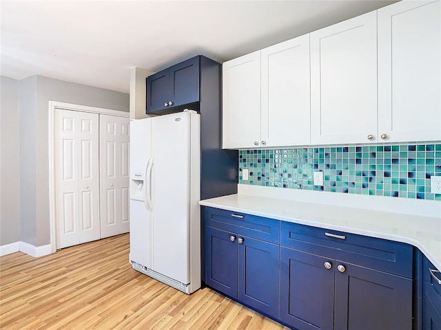 kitchen with light hardwood / wood-style flooring, backsplash, white fridge with ice dispenser, blue cabinetry, and white cabinetry