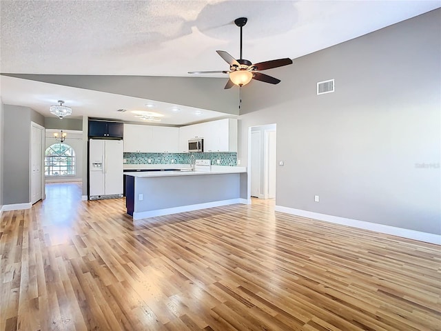 kitchen with white cabinetry, white fridge with ice dispenser, lofted ceiling, tasteful backsplash, and ceiling fan with notable chandelier