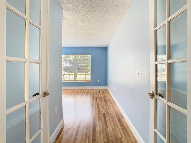 corridor with a textured ceiling, french doors, and hardwood / wood-style flooring