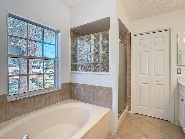 bathroom featuring plus walk in shower, vanity, a textured ceiling, and tile patterned floors