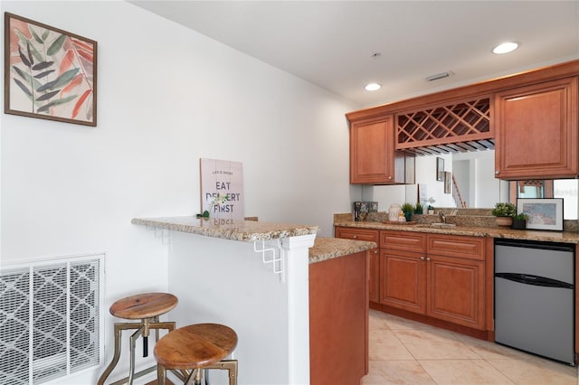 kitchen with light stone countertops, a kitchen bar, a peninsula, and brown cabinetry