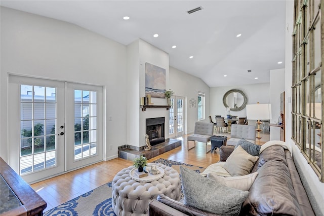 living room with visible vents, light wood-style flooring, french doors, a fireplace, and high vaulted ceiling